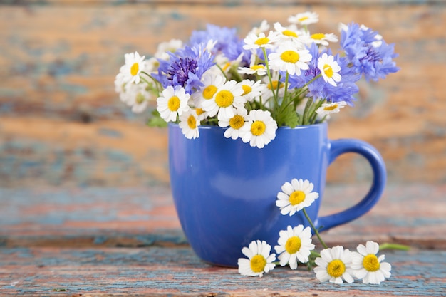 Blue cup with a bouquet of daisies and cornflowers on an old wooden background