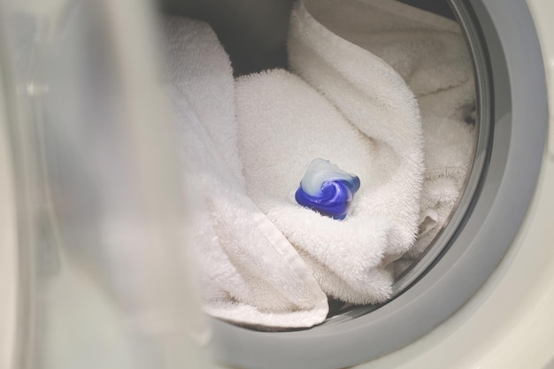 Blue detergent pod capsule for washing clothes lies in the washing machine on white cotton towels