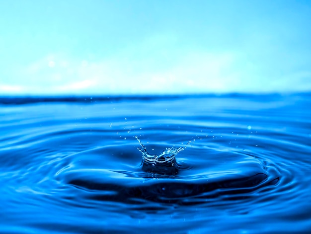 A blue drop drips into the water and creates splashes of various shapes, waves are created through the water, the concept of a liquid splash, a substance painted in blue color