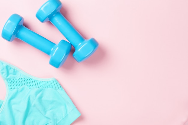 Blue dumbbells and sport bra on a pink background