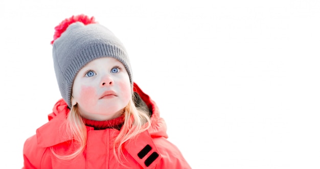 A blue-eyed little girl in a knitted hat and a pink winter jacket looks up. Close up, isolated on white