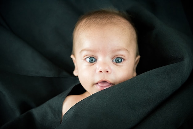 Blue eyed naked baby lying on black fabric