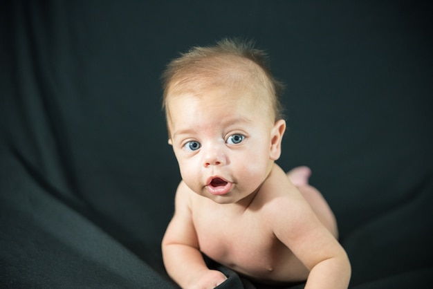 Blue eyed naked baby lying on black fabric