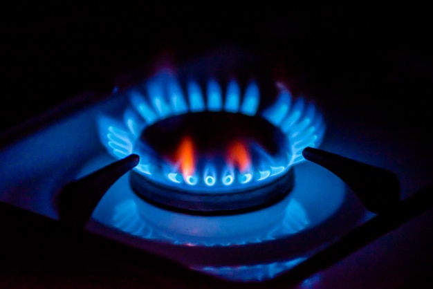 A blue flame of a gas stove is lit up in the dark.