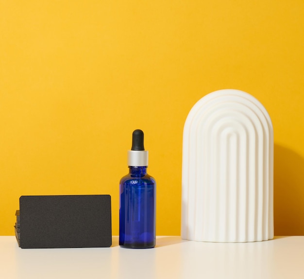 Blue glass bottle with pipette stands on a white table. Cosmetics SPA branding. Packaging for gel, serum, advertising and product promotion, mock up