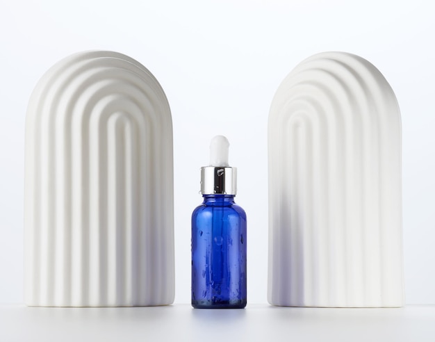 blue glass bottle with a pipette and white decorative arches on a white background. Template for cosmetic liquid products, advertising and promotion