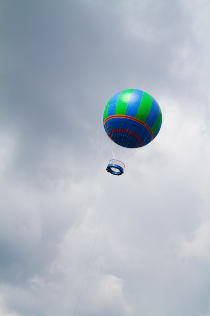 A blue and green hot air baloon rises into an ominously gray cloudy sky