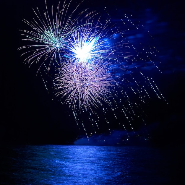 Blue holiday fireworks above lake with water reflection and black sky