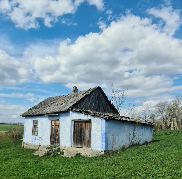 A blue house in a field with a cloudy sky behind it.