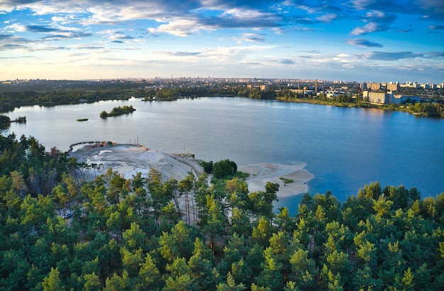 Blue lake, pine forest, big city and beautiful sky with clouds in one photo