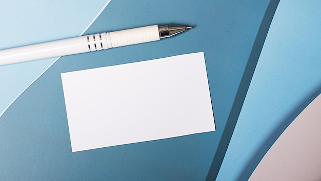 On a blue, light blue and pink background, there is a white blank card with a place to insert text on a paper clip and a white pen. Multi-layered background. Template