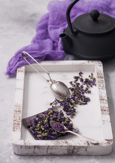 Blue mallow flowers tea in steel plate with vintage strainer infuser in wooden box with teapot and purple cloth on white background