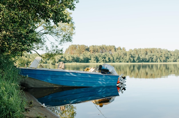 Blue motorboat parked near shore of lake on sunny summer day Side view of simple fishing boat on water