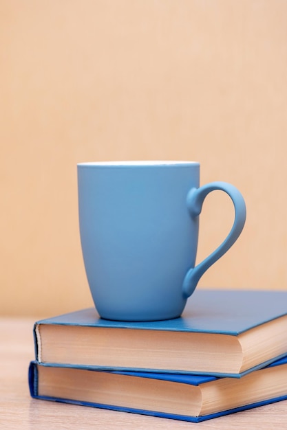 A blue mug and books with a blue hardcover on a wooden table. vertical photo