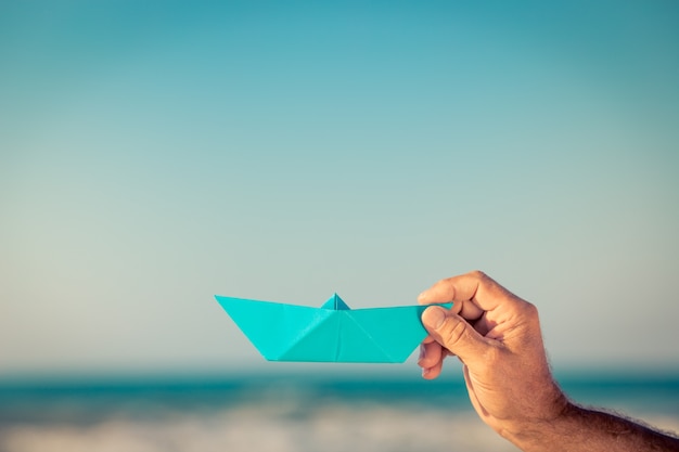 Blue origami paper boat being hold by a hand with sea background