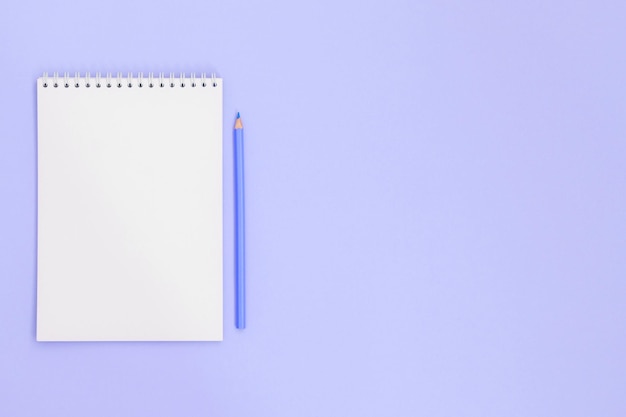 Blue pencil near a notebook, on a violet background. There is room for text, copy space.