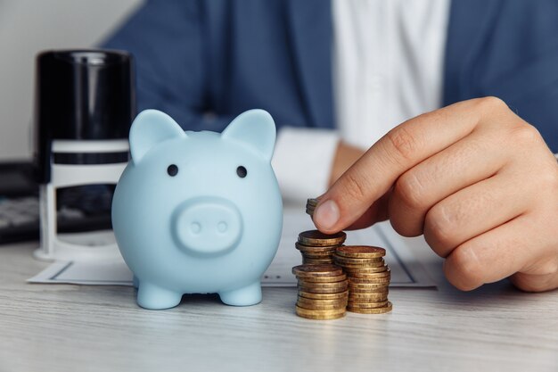 Blue piggy bank stamp and mans fingers with coins on desk in office