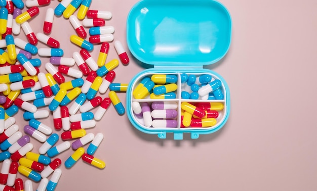 A blue pill container with pills on a pink background