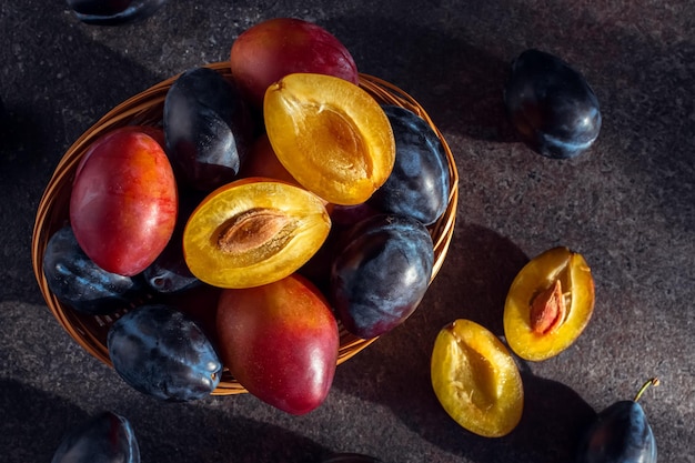 Photo blue and pink plums cut plums on a dark table