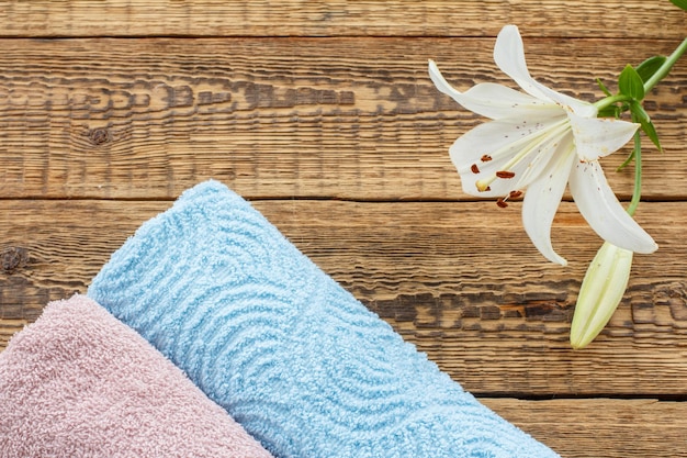 Blue and pink soft terry towels with white lily flower on old wooden boards Top view with copy space