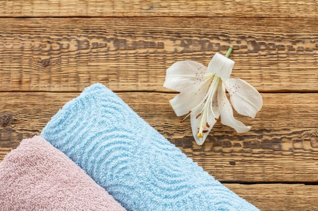 Blue and pink soft terry towels with white lily flower on old wooden boards. Top view.