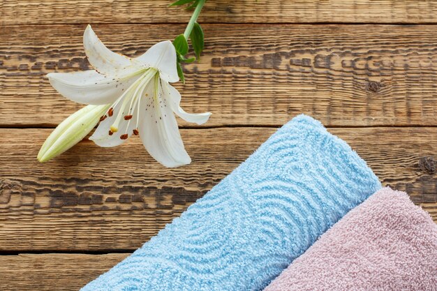 Blue and pink soft terry towels with white lily flower on old wooden boards. Top view.