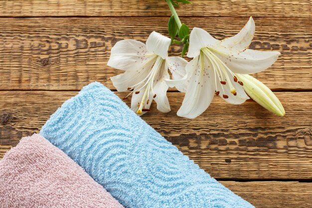 Blue and pink soft terry towels with white lily flowers on old wooden boards. Top view.