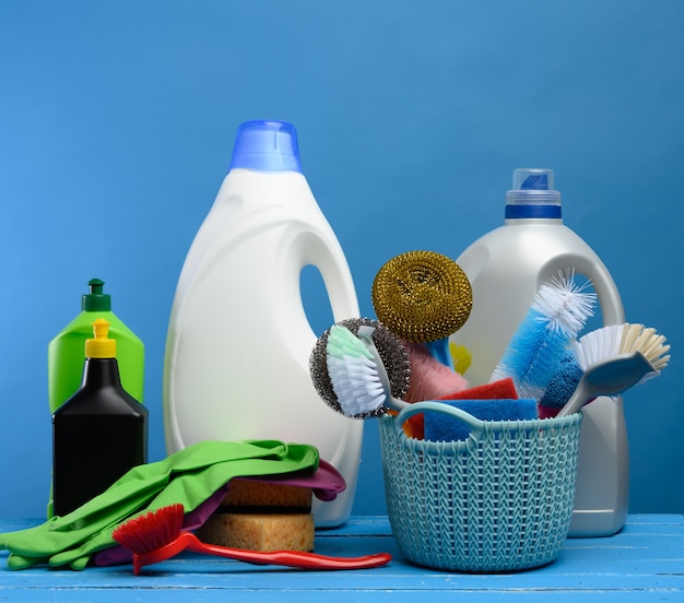 Blue plastic basket with brushes, sponges and rubber gloves for cleaning the premises, next to a bottle of detergent, blue background