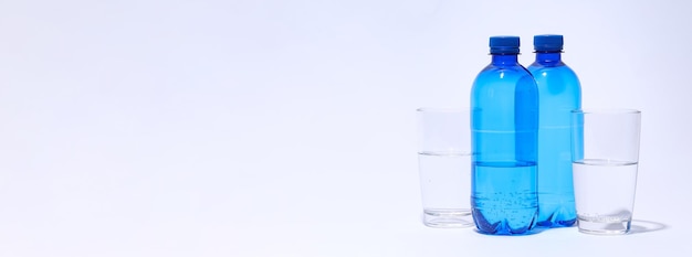 Blue plastic bottles and glasses of water on light background