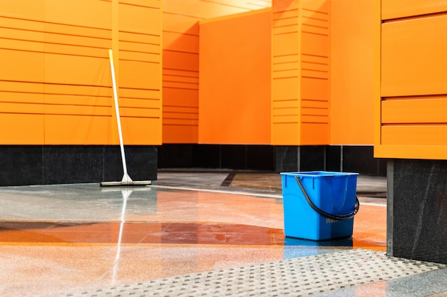 Blue plastic bucket and mop on empty subway station with orange walls.