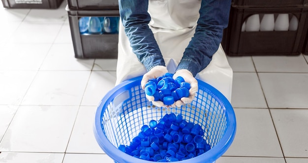 Blue plastic water bottle cap in hand worker or quality inspector in workwear in drink water factory