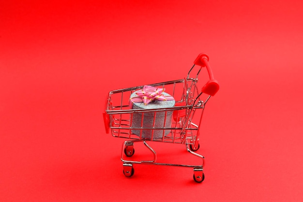 Blue present box with pink bow in a shopping cart on a red background