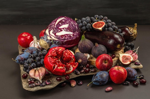 Blue, red and purple food. Culinary background of fruits and vegetables. Fresh figs, plums, onions, eggplant, grapes, cabbage, apples, garlic, dogwood, pomegranate. Black stone background, flat lay