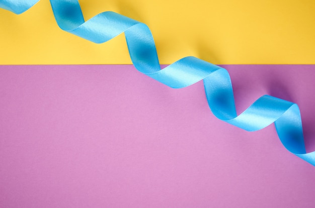 Blue ribbon on purple and yellow background with copyspace, flat lay