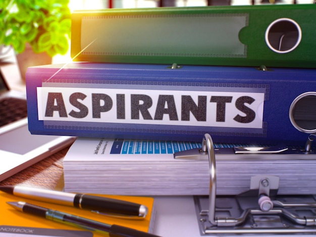 Blue Ring Binder with Inscription Aspirants on Background of Working Table with Office Supplies and Laptop Aspirants Business Concept on Blurred Background 3D Render