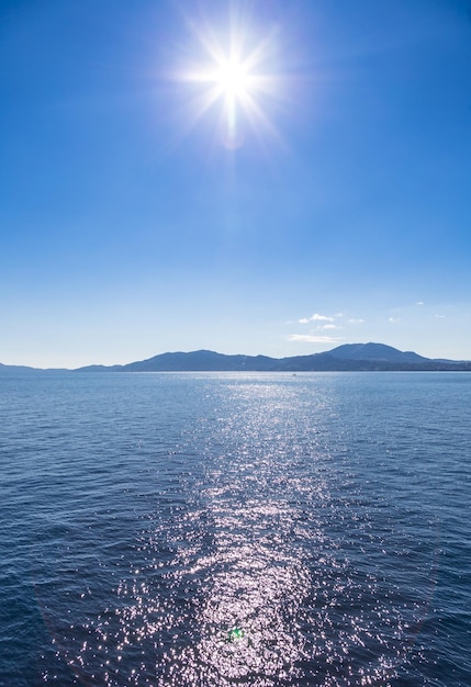 Blue sea waters and clear blue sky with sun flare