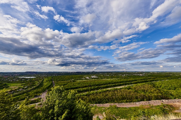 Blue sky with clouds above the green trees outside the city in the sunlight.