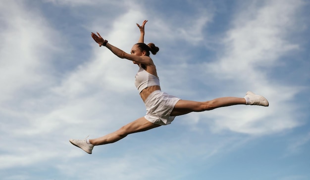 Photo blue sky with clouds jumping young skinny fitness woman is outdoors