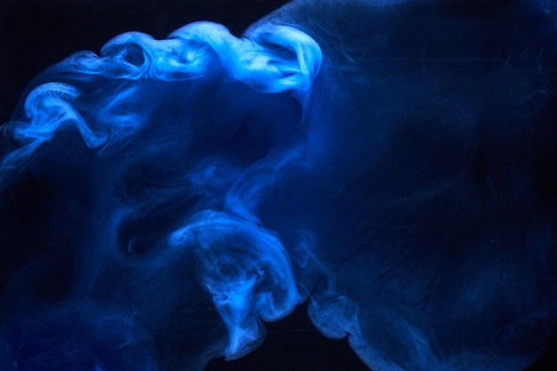 Blue smoke on black ink background, colorful fog, abstract swirling ocean sea, acrylic paint pigment underwater