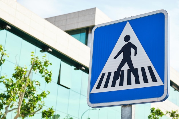 Blue square crosswalk traffic sign with glass building in the background