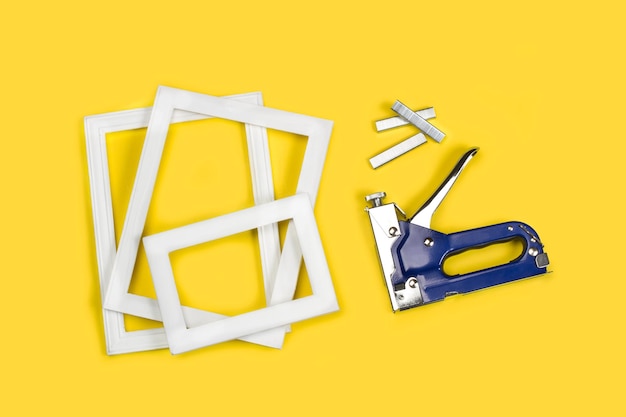 A blue stapler gun, staples and photo frames on a yellow background with copy space