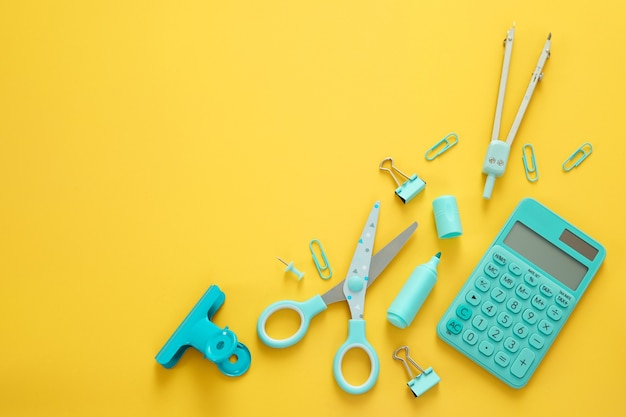 Blue stationery items on the yellow background with free space for text. Creative, colorful background with school supplies. Flatlay with copy space, top view. Marker, pen, paper clips, scissors.