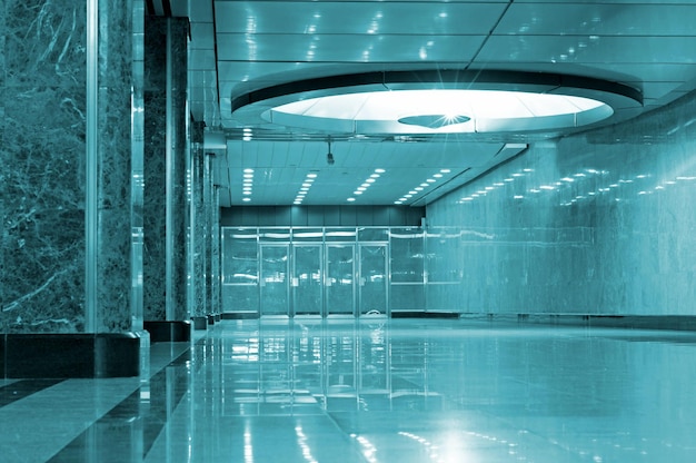 A blue subway station with a glass ceiling and a light on the ceiling.