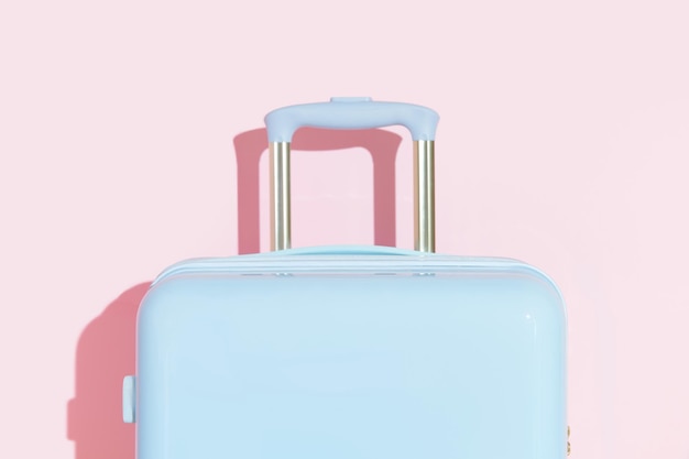 Blue suitcase on a pastel pink background with long deep shadows Travel concept Minimal style