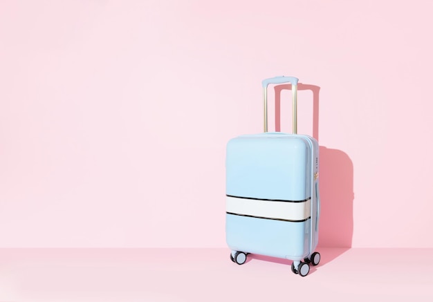 Blue suitcase on a pastel pink background with long deep shadows Travel concept Minimal style