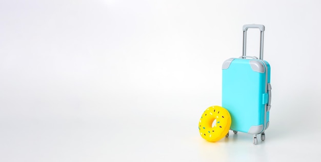 A blue suitcase on wheels and a yellow inflatable donut stand on a white wide background