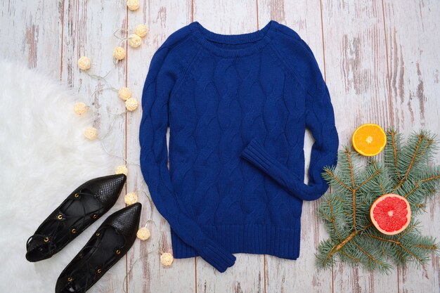 Blue sweater with braids and black shoes. Citrus, fir branch garland.