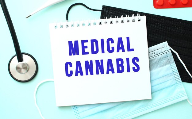 The blue text medical cannabis is written in a notebook that lies on a blue background next to a med...