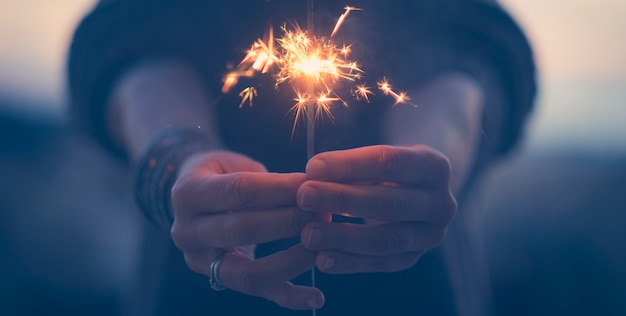 Blue tones of hands of woman holding sparkler light during new year celebration