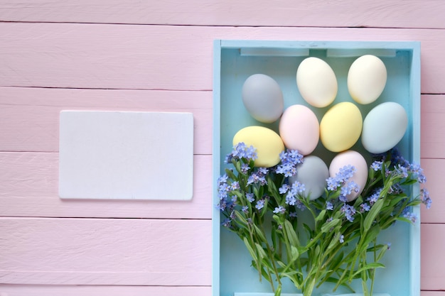 Blue tray with easter decorative eggs in pastel colors and forget-me-not flowers on light pink pastel board